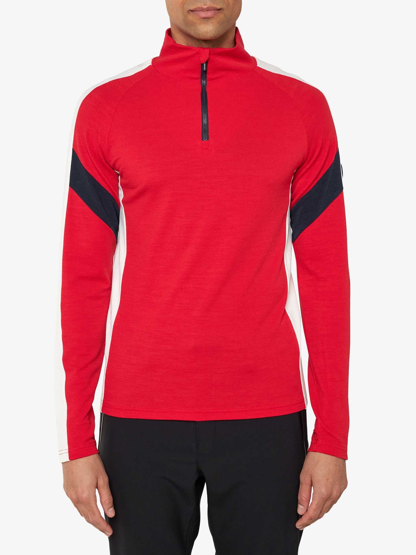 A person is wearing a red, long-sleeve Zermatt Zipup Men from We Norwegians, made of superfine Merino wool, featuring black and white stripes on the sleeves. They are also wearing black pants. The background is plain white.