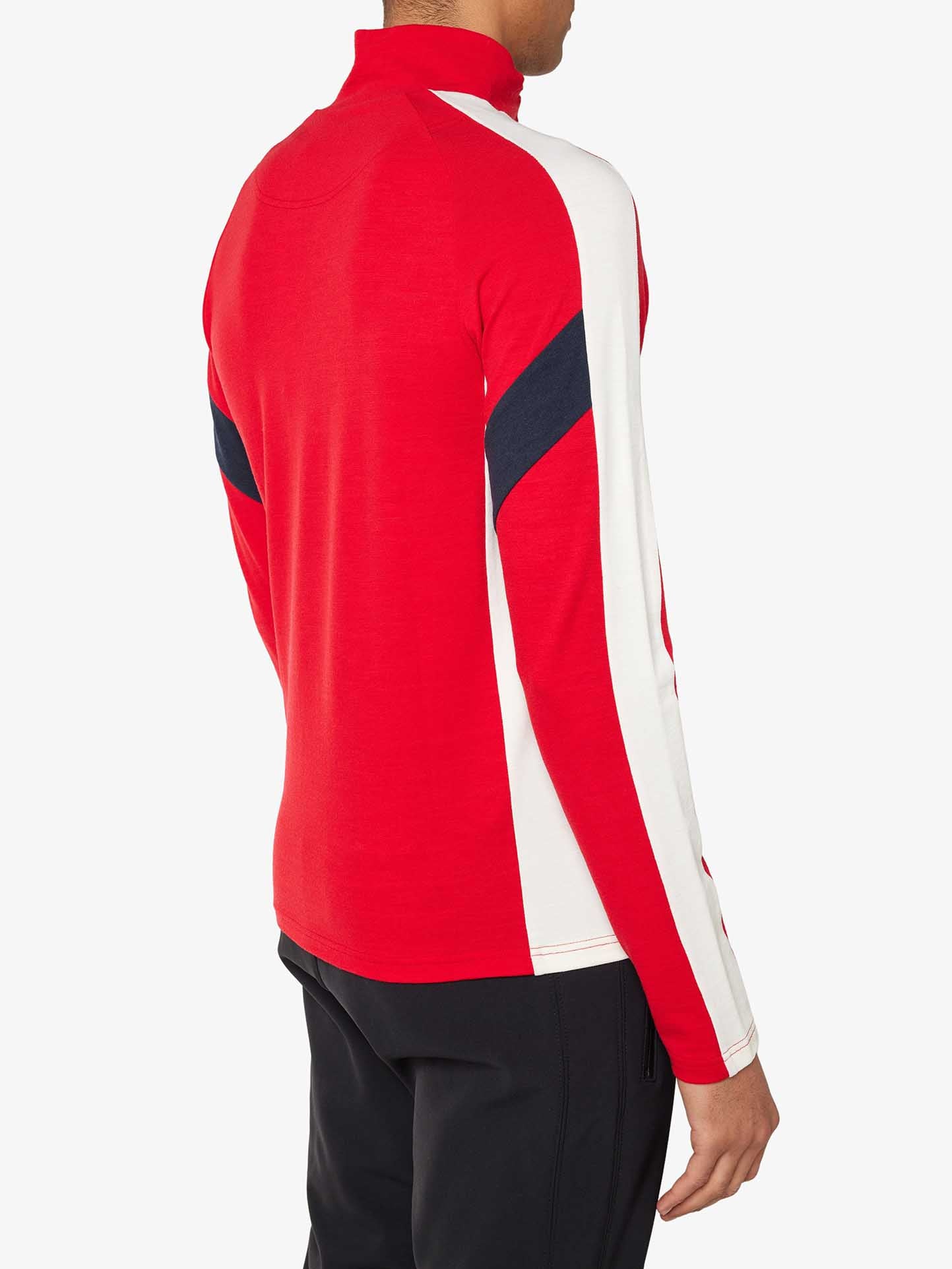 A person is wearing a long-sleeved, red and white Zermatt Zipup Men top from We Norwegians, featuring a collar and a navy blue diagonal stripe on the sleeves and back. The top is knitted from superfine Merino wool. The person is also wearing black pants. The image is taken from the back, focusing on the upper body and torso.