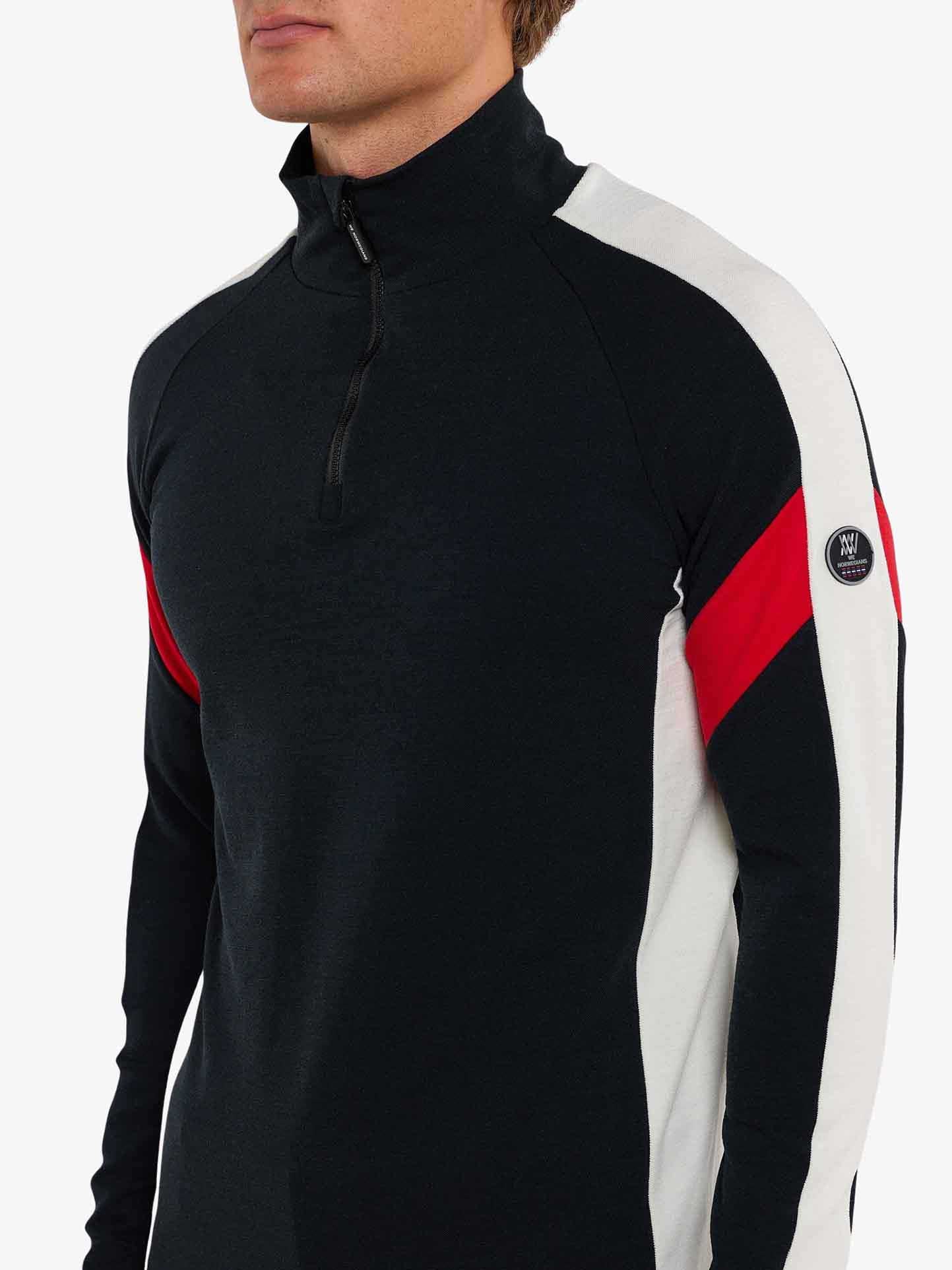 A person wearing a sleek black Zermatt Zipup Men athletic top from We Norwegians, featuring striking white sleeves and red accents. The We Norwegians brand logo is prominently displayed on the upper part of the left sleeve, adding a touch of premium elegance. The plain white background accentuates the sophistication and durability of this ski ensemble.