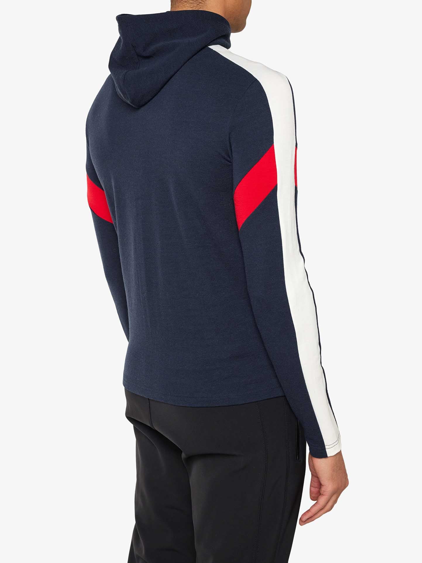 A person is wearing a navy Zermatt Fullzip Hoodie Men from We Norwegians, featuring white sleeves and red stripes running diagonally across the upper arms. The athletic fit hoodie showcases the back, as they are facing away from the camera, paired with black pants.