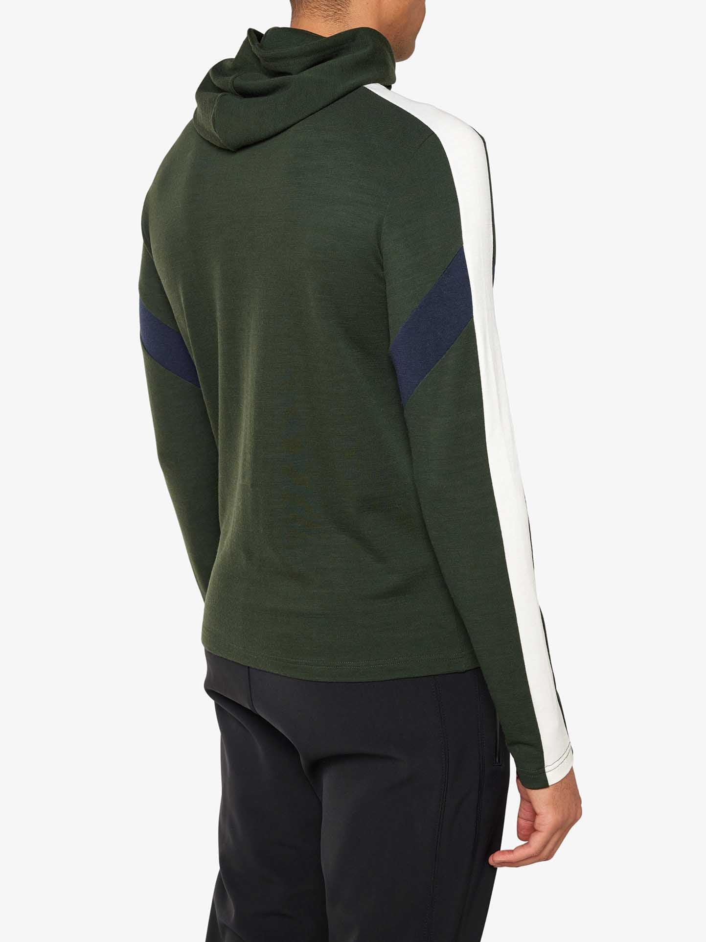 A person is wearing a green Zermatt Fullzip Hoodie Men from We Norwegians, featuring white and navy blue stripes on the sleeves. The athletic fit hoodie, viewed from the back, pairs perfectly with their black pants. The plain white background highlights the stylish yet practical ensemble.