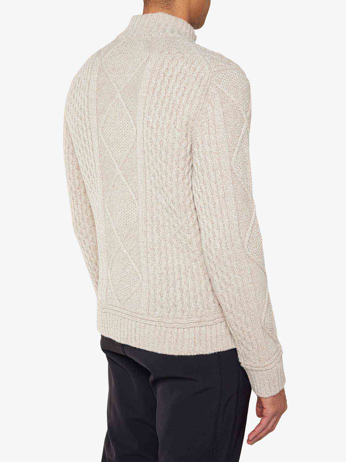 A person is seen from the back wearing the We Norwegians Geilo Cableknit 1/4-Zip Men cardigan, made of Italian yarn in a cream color with a diamond pattern. The individual is also dressed in black pants, and the background is plain white.