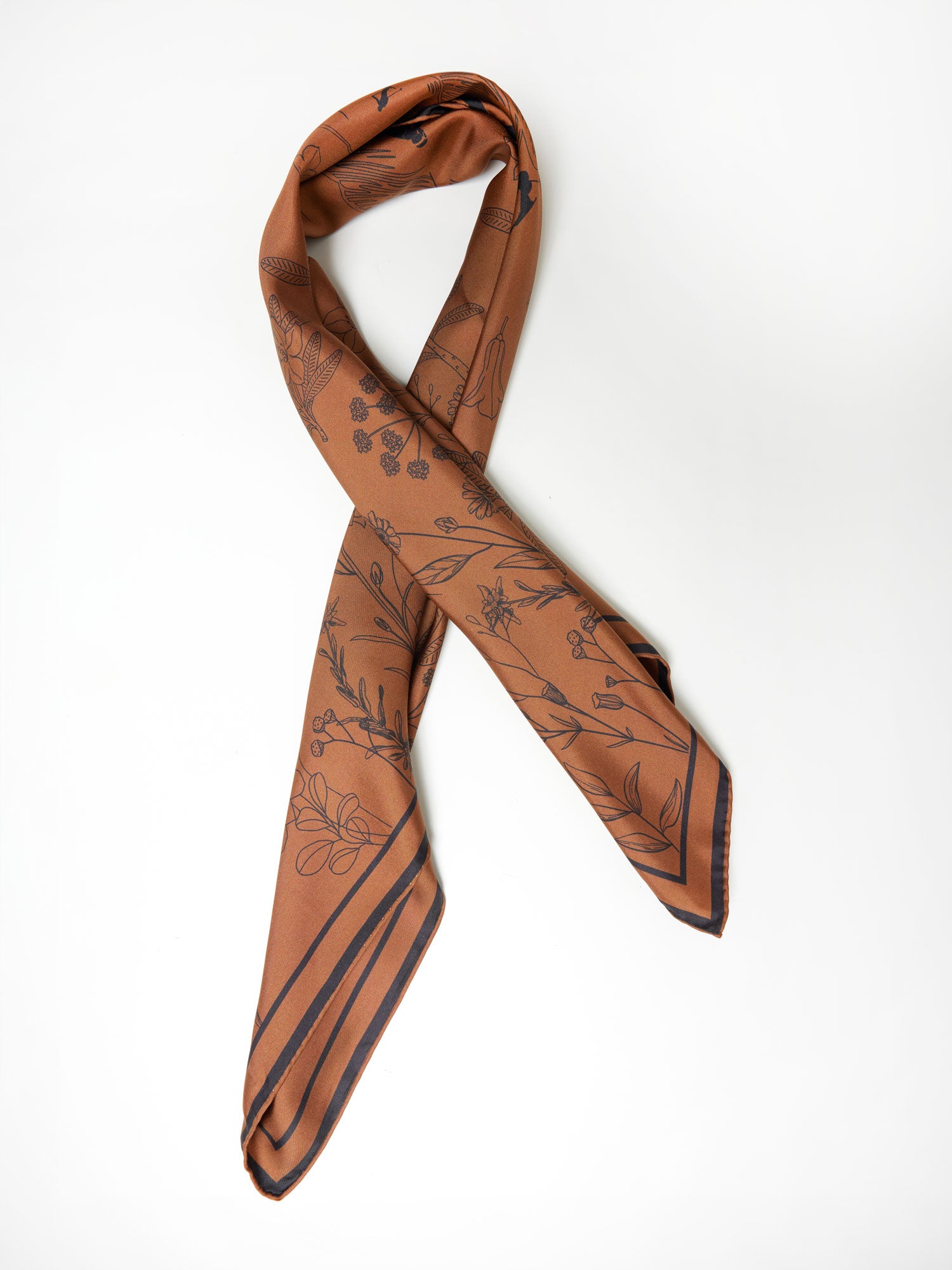 A pure silk scarf in brown with black printed floral and leaf patterns is neatly folded in a looped design against a plain white background. This We Norwegians Alps Silk Scarf, featuring diagonal black stripes near the edges, would be a perfect addition to your ski outfit.