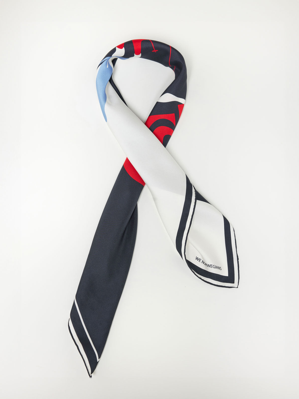 A stylish silk scarf with a modern, abstract design, the Afterski Silk Scarf features a mix of red, blue, black, and white colors with a contrasting border. The brand name "We Norwegians" is printed on one end. Styled against a white background, it pairs seamlessly with your retro color block panels wardrobe.