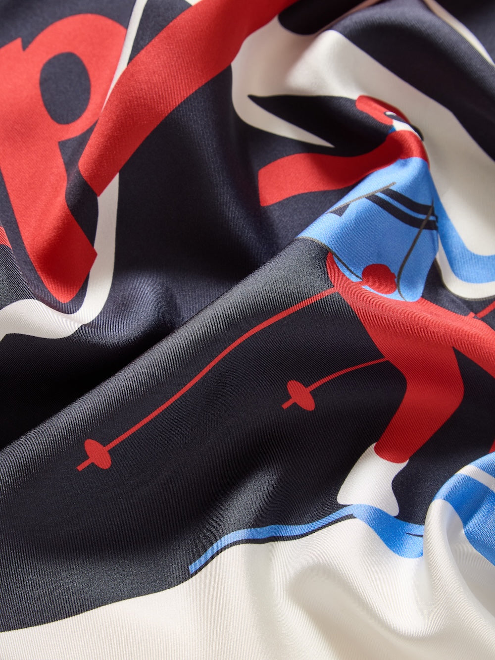 A close-up of the Afterski Silk Scarf by We Norwegians reveals its silky twill texture and vibrant abstract print in red, black, blue, and white shapes and lines, slightly wrinkled—showcasing the scarf’s refined allure and delicate hand-stitched edges.