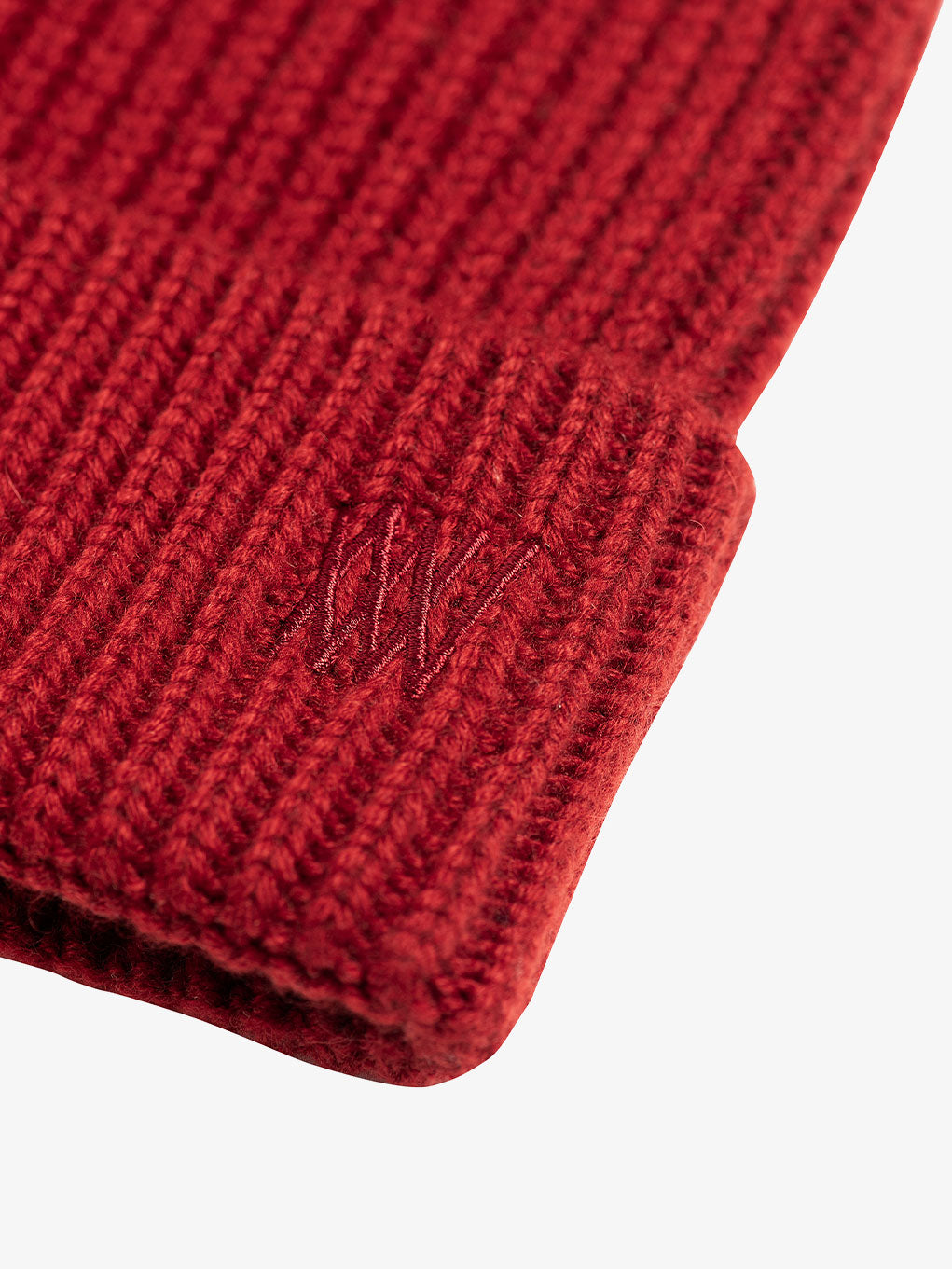 Close-up of a red ribbed Blefjell Hat from We Norwegians featuring tonal embroidered initials "WW" on the adjustable cuff. The texture of the knit fabric is visible, emphasizing the warm and cozy appearance of this luxurious beanie.