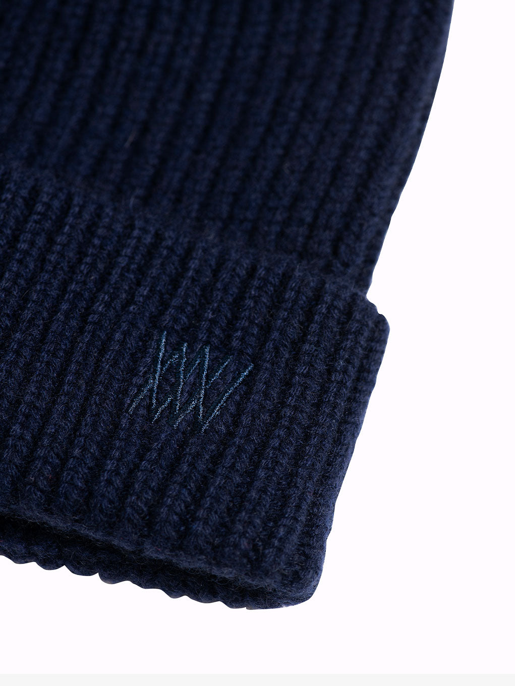 Close-up of the We Norwegians Blefjell Hat, featuring a dark blue ribbed knit design with tonal embroidery of three overlapping lines in matching color on the adjustable cuff. The background is plain white.