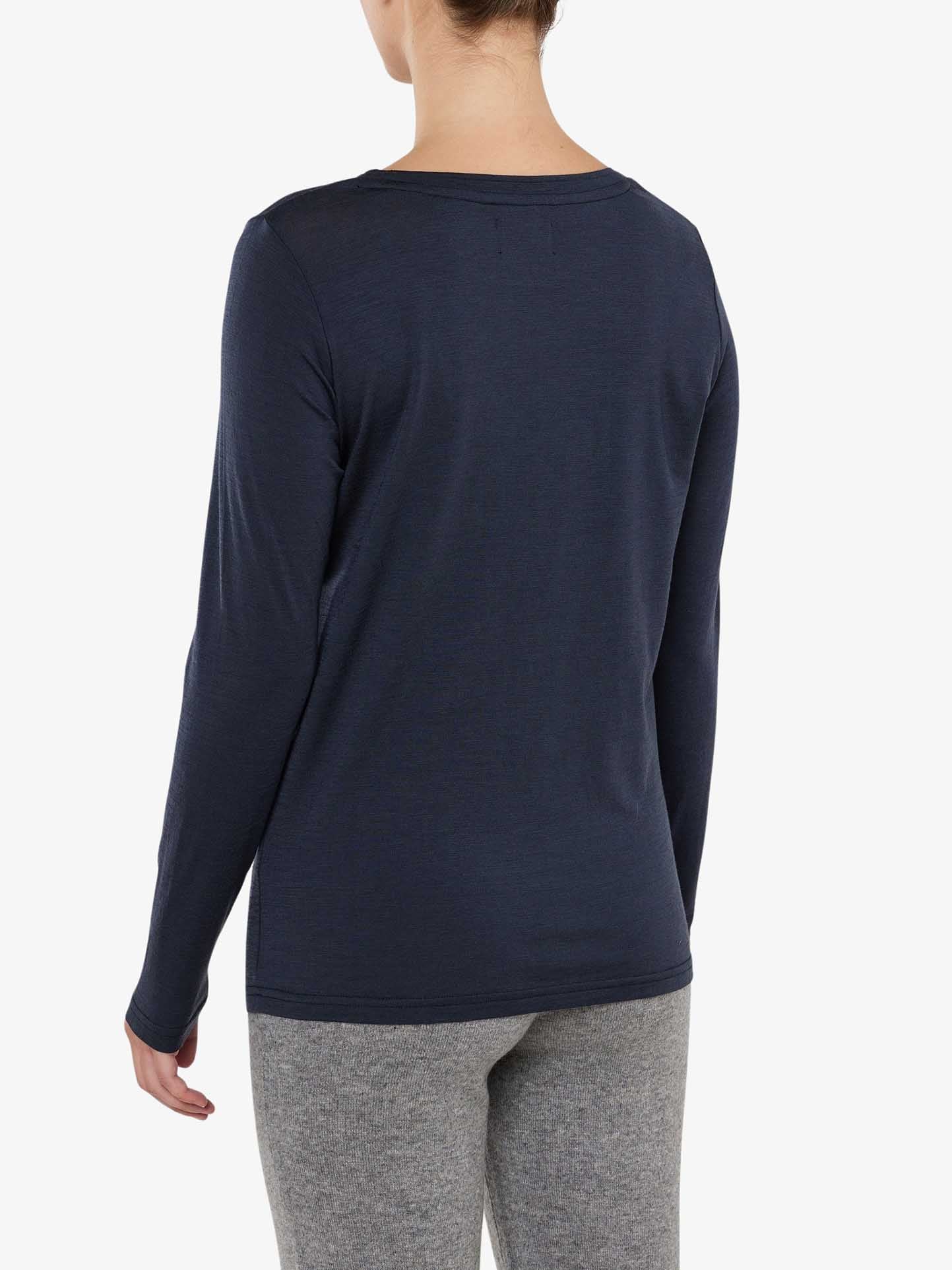 A person stands with their back to the camera, wearing the We Norwegians Berg LongSleeve Women shirt in navy blue and gray pants. The person has short hair, and their right hand is partially visible by their side. The background is plain white.