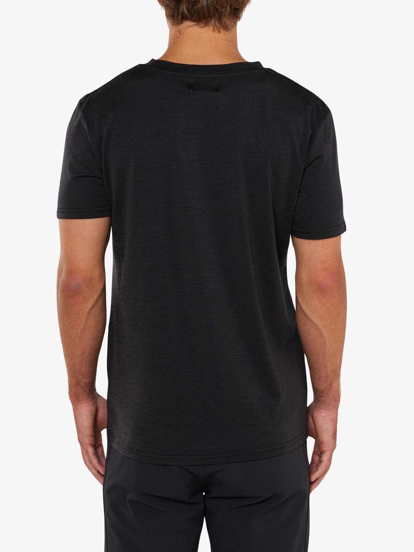 A person with short hair is standing with their back to the camera, wearing a plain black Berg Tee Men by We Norwegians and black pants. The background is plain white.