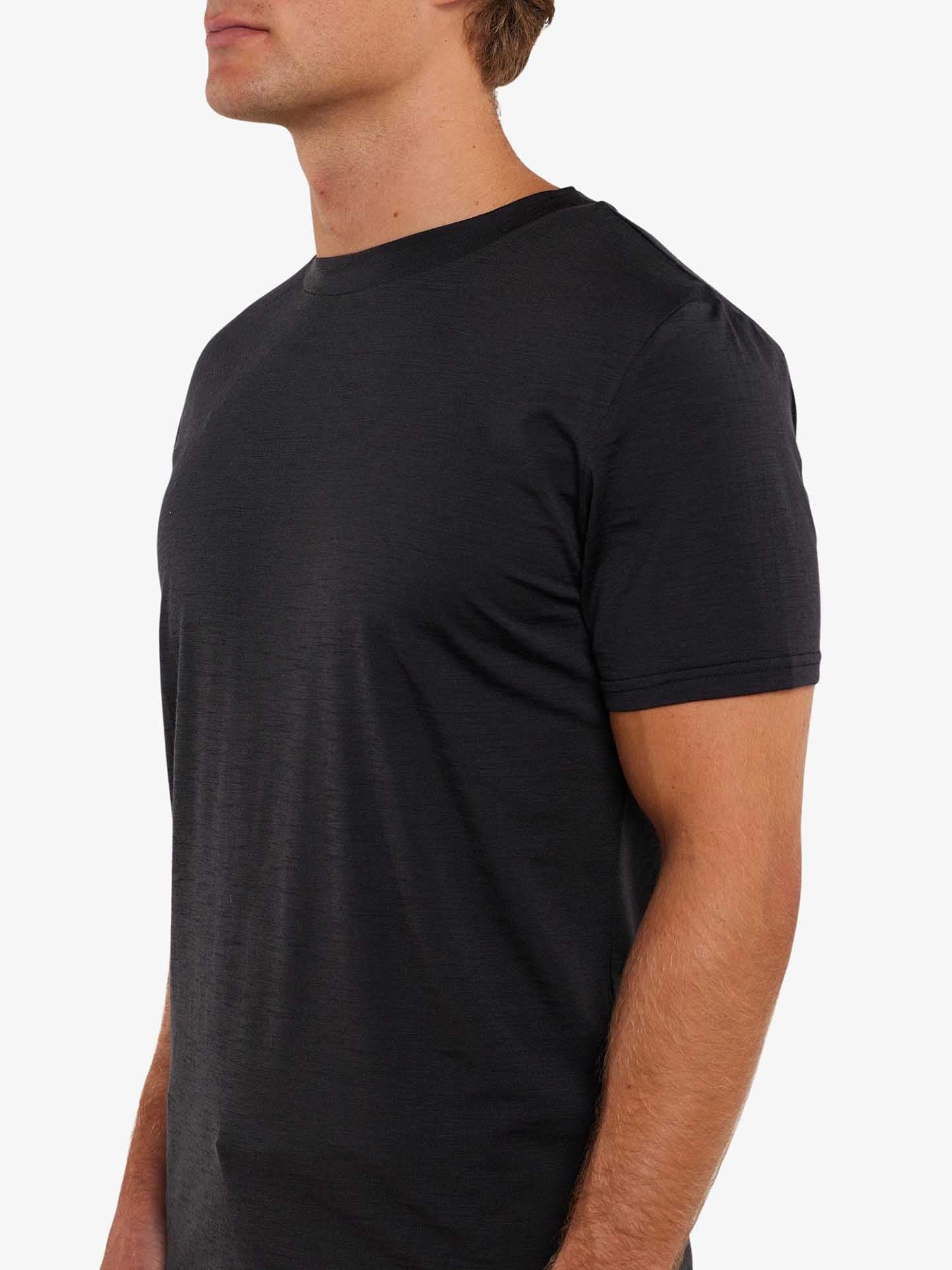 A man is wearing a plain black Berg Tee Men by We Norwegians, made from soft Merino wool. The image is a side profile view, showing the upper half of his body against a plain, light-colored background.