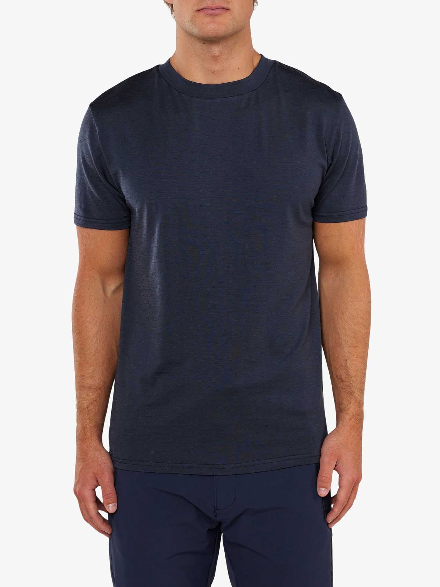 A person wearing a plain, dark-colored, short-sleeve Berg Tee Men by We Norwegians and dark pants is standing against a white background. The t-shirt has a crew neck and a simple, minimalist design.