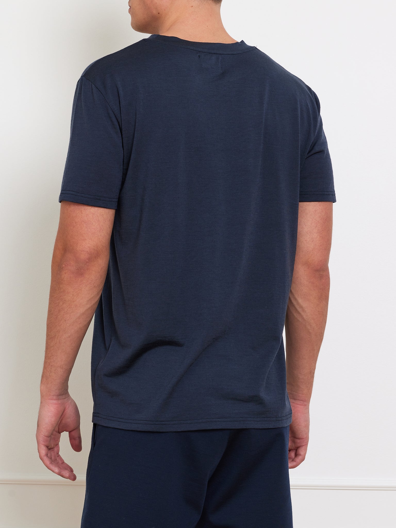 A person in a plain Berg Tee Men by We Norwegians and matching pants, crafted from cooling fabric, stands facing away against a white background with arms relaxed by their sides.