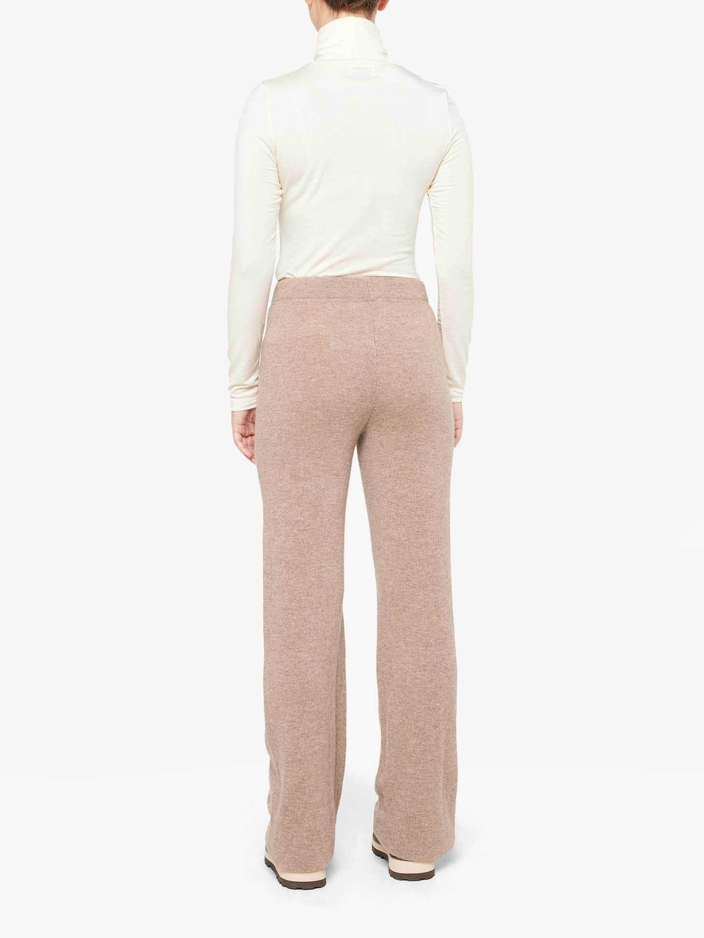 A person wearing a white turtleneck and the Blefjell Cashmere Pant Women from We Norwegians stands with their back to the camera. The outfit, crafted from 100% cashmere, radiates comfort and casual elegance.