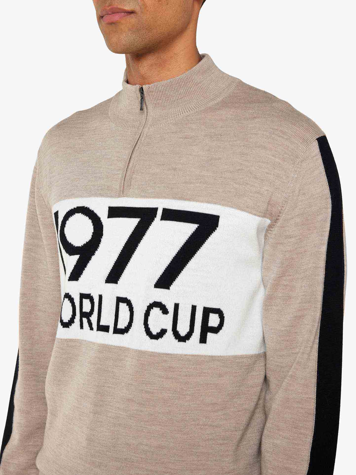 A person wears the We Norwegians 1977 World Cup Zipup Men sweater, channeling 70s ski style. The beige quarter-zip features a striking white chest panel with "1977 WORLD CUP," evoking Ingemar Stenmark’s era against a timeless gray background.