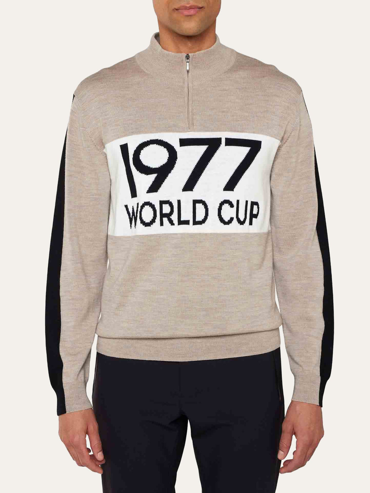 Wearing the We Norwegians World Cup Zipup Men, this person sports a beige quarter-zip sweater featuring black sleeves and a white chest panel boldly printed with “1977 WORLD CUP,” channeling authentic 70s skiing style.