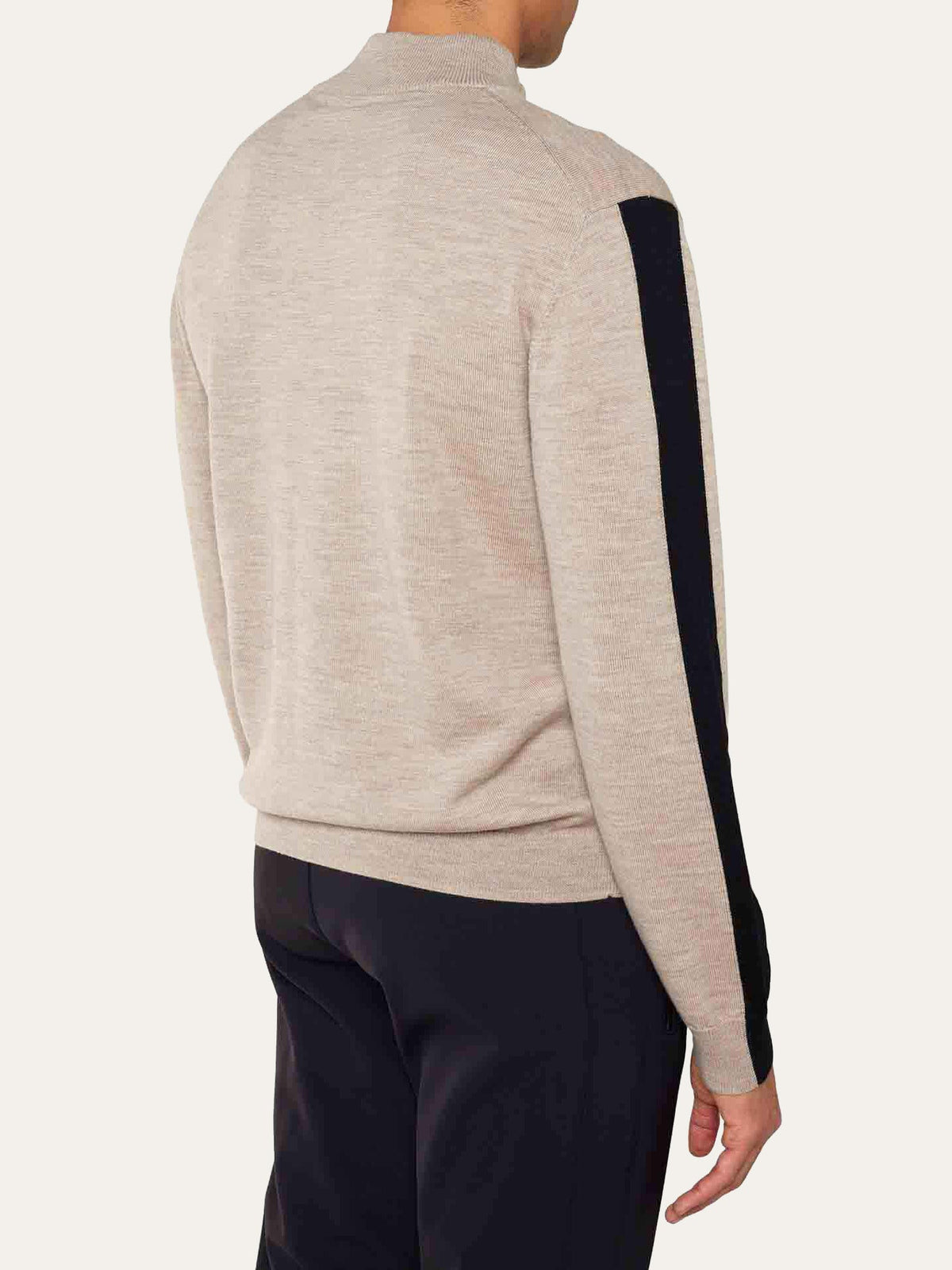 A person is shown from the back, standing against a plain background, wearing the We Norwegians World Cup Zipup Men sweater in beige with a black stripe down the sleeve, paired with dark pants.