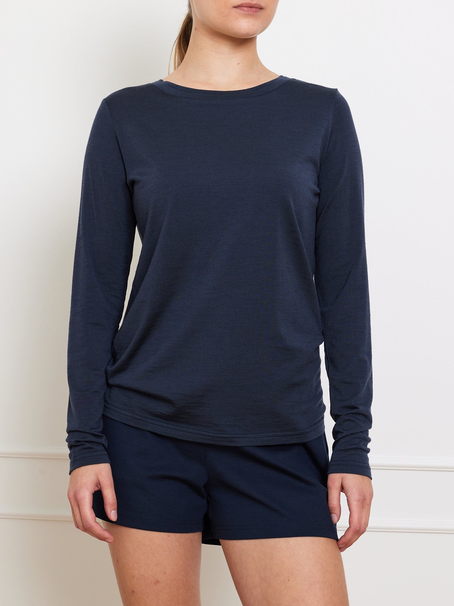 A person in a We Norwegians Berg LongSleeve Women shirt and matching shorts stands against a white background. The head is cropped, highlighting the sleek design and eco-friendly Tencel fabric of the outfit.