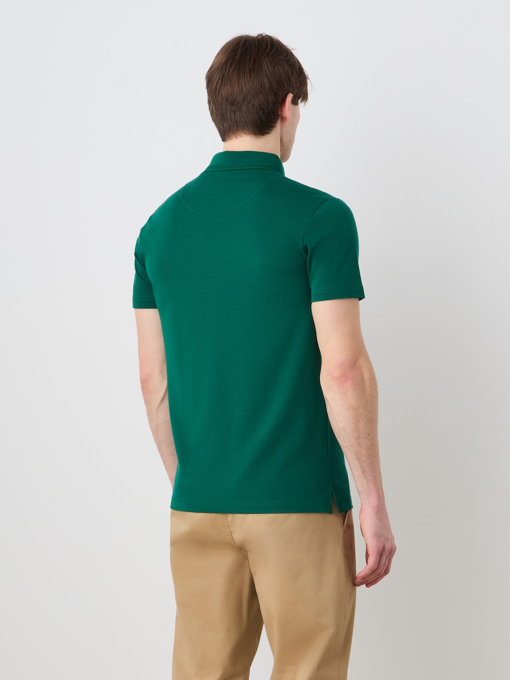 A man with short brown hair stands with his back to the camera, wearing the We Norwegians Medalist Piqué Polo Men in green and beige pants against a plain white background.