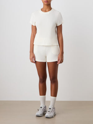 A person stands indoors in We Norwegians Waffle Shorts for women, paired with a matching white ribbed short-sleeve top, white socks, and light gray athletic sneakers against a plain light-colored background.