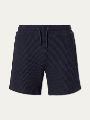 We Norwegians Waffle Shorts Men in navy blue cotton feature a relaxed fit, adjustable drawstring waistband, and side pockets, shown against a plain light background.