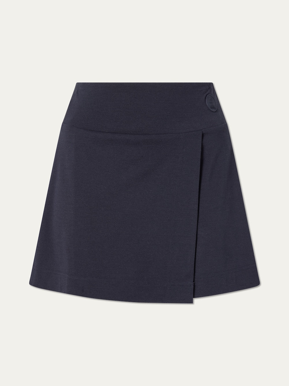 The We Norwegians Medalist Piqué Skirt Women features an A-line navy design in merino wool with a subtle overlapping front panel, a small round button at the waistband, and minimalist style for versatile wear beyond the classic tennis skirt.