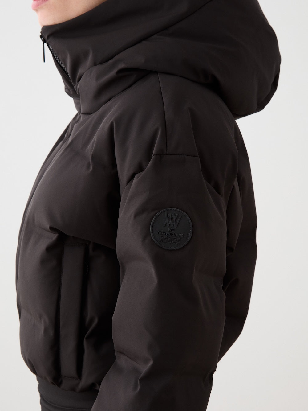 A model wearing the We Norwegians Aurora Ski Suit for women, shown from the side against a plain light background, featuring an effortless alpine style.