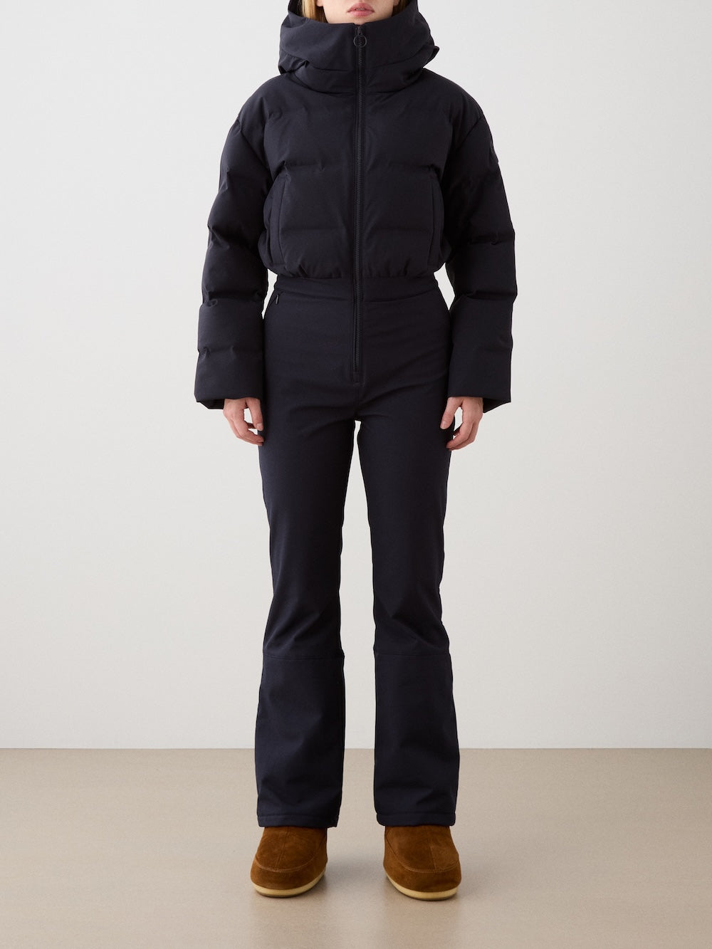 A person stands against a plain background wearing the Aurora Ski Suit for women by We Norwegians. Their hands hang by their sides and their head is partially out of frame.