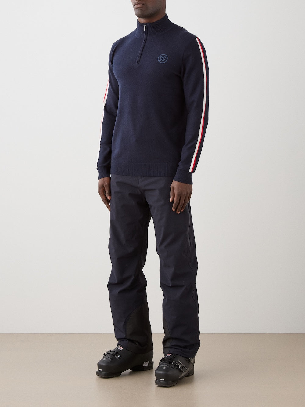 Model is wearing The FreeBird ZipUp men by We Norwegians is a navy blue lightweight sweater with red and white sleeve stripes and a small circular embroidered logo on the left chest.