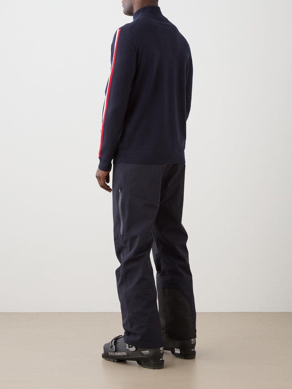 Model is wearing The FreeBird ZipUp men by We Norwegians is a navy blue lightweight sweater with red and white sleeve stripes and a small circular embroidered logo on the left chest.