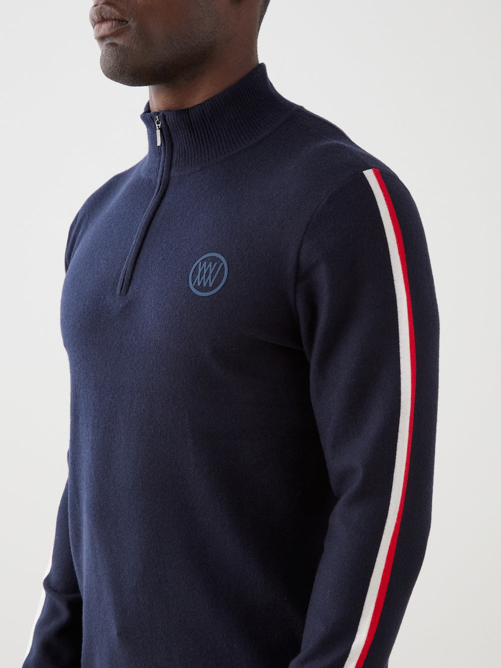 Model is wearing The FreeBird ZipUp men by We Norwegians is a navy blue lightweight sweater with red and white sleeve stripes and a small circular embroidered logo on the left chest.