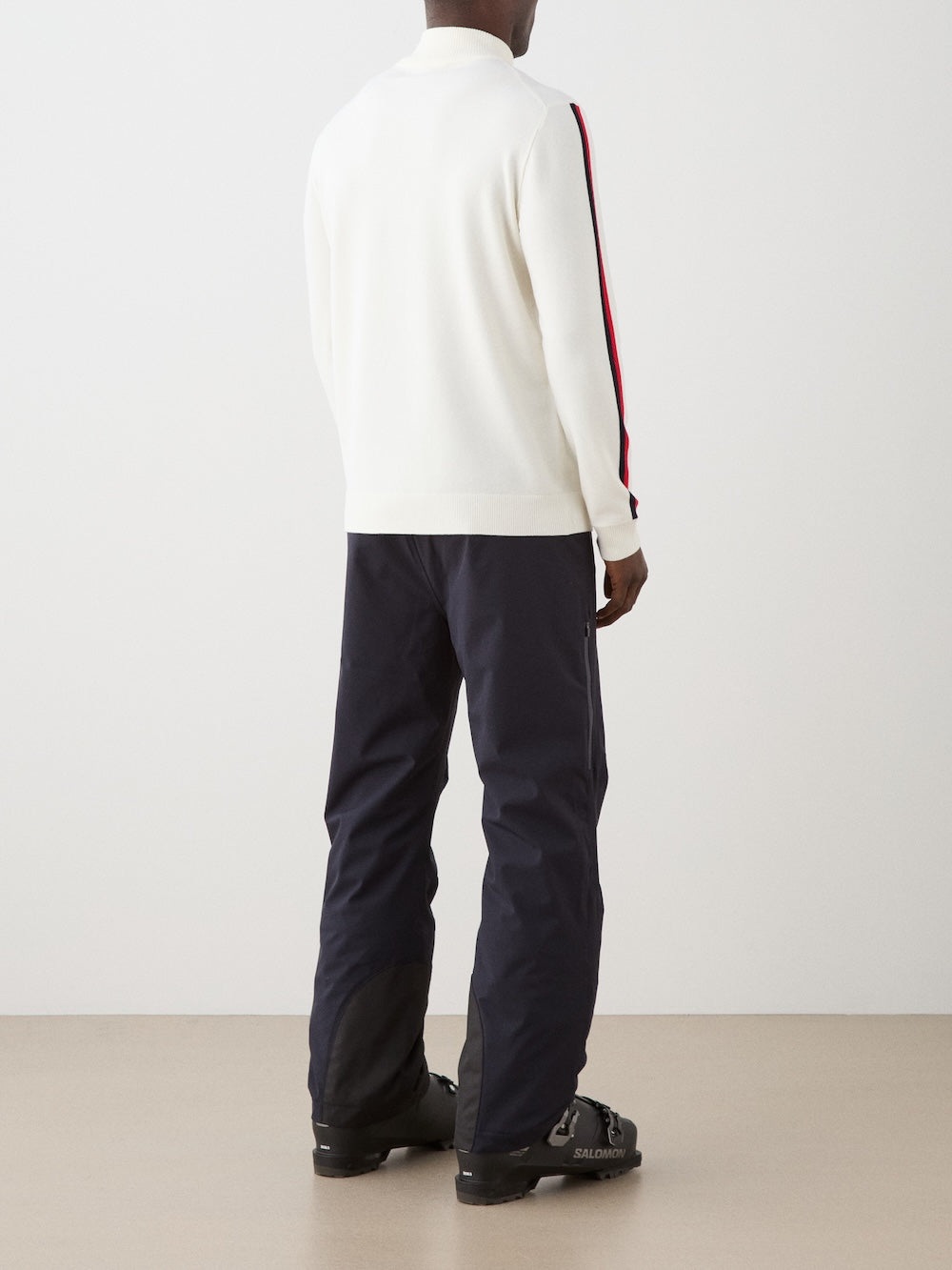 Model is wearing The We Norwegians FreeBird ZipUp men is a cream-colored, lightweight quarter-zip sweater with red and black sleeve stripes and a white circular chest logo—a modern update of the classic ski sweater.