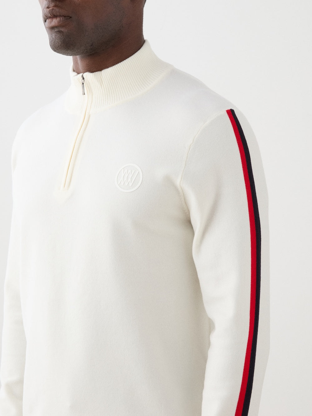 Model is wearing The We Norwegians FreeBird ZipUp men is a cream-colored, lightweight quarter-zip sweater with red and black sleeve stripes and a white circular chest logo—a modern update of the classic ski sweater.