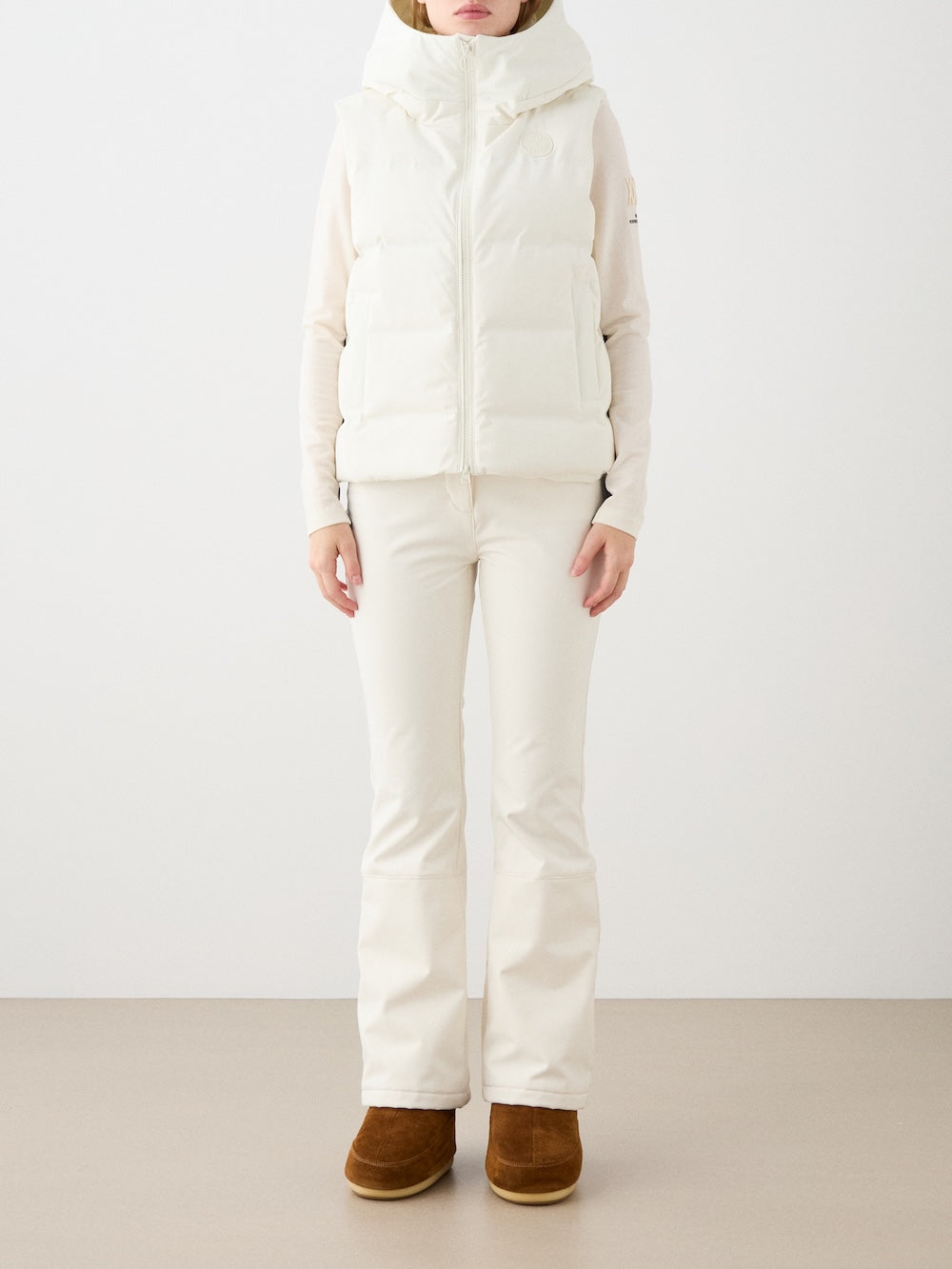 A person stands against a plain background wearing the We Norwegians Aurora Vest women in white, paired with a white long-sleeve top, white pants, and brown boots for a minimalist Scandinavian look. Face not visible.