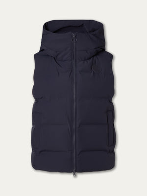 The We Norwegians Aurora Vest women is a sleeveless dark navy puffer with a hood, front zipper, and two side pockets, displayed on an off-white background for a refined Scandinavian look.