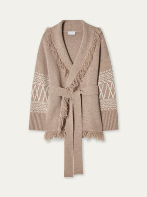 The We Norwegians Setesdal Cardigan women is crafted from a luxurious merino-cashmere blend and features a beige knit design with a shawl collar, fringe trim, white geometric Norwegian-inspired patterns along the sleeves, ribbed cuffs, and a matching belt cinched at the waist, showcased against a light background.