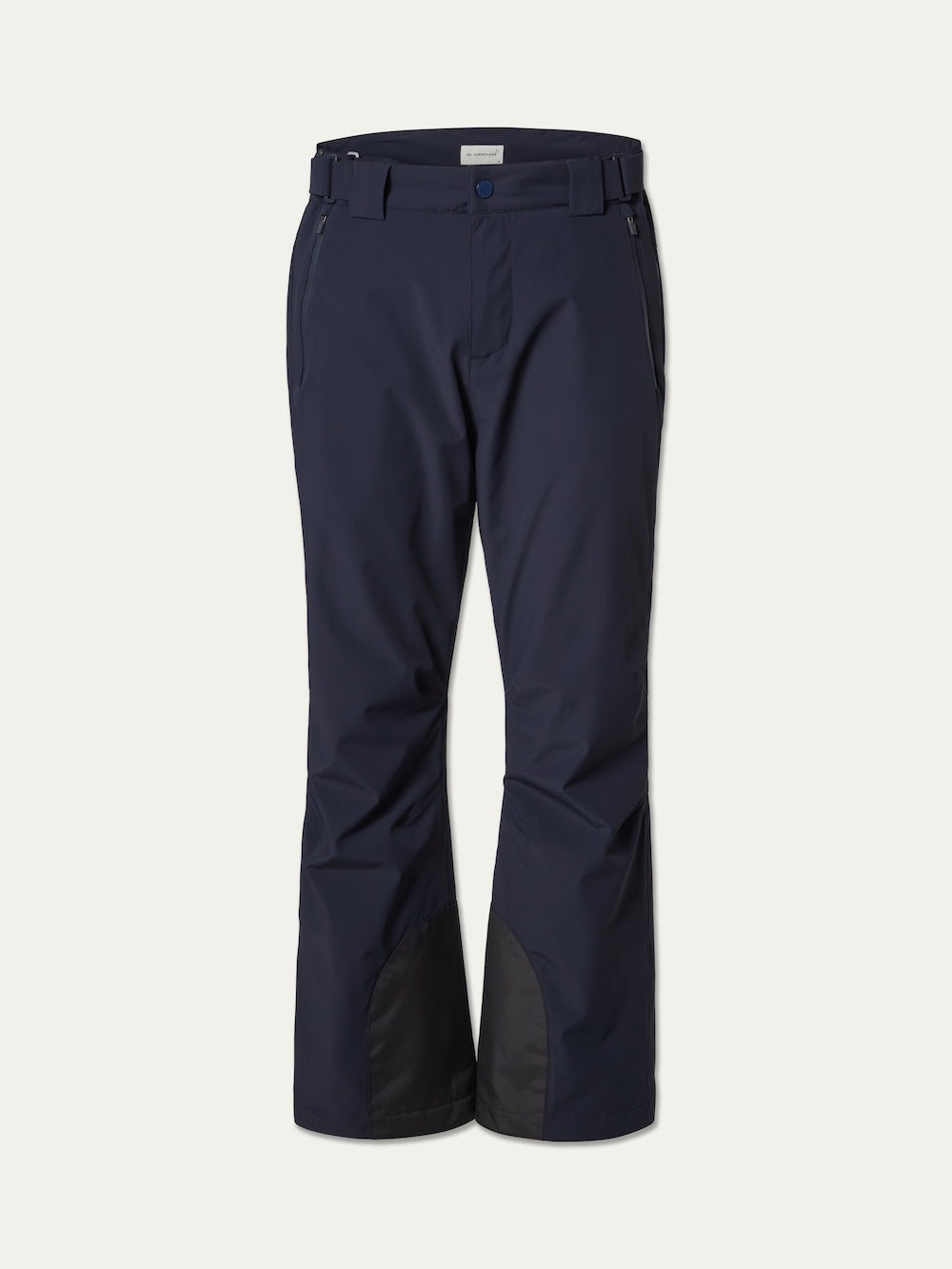 The Hammerfest Ski Pant men by We Norwegians features a navy blue color, 4-way stretch fabric, side pockets, belt loops, a front button closure, and reinforced black fabric patches on the inner lower legs.