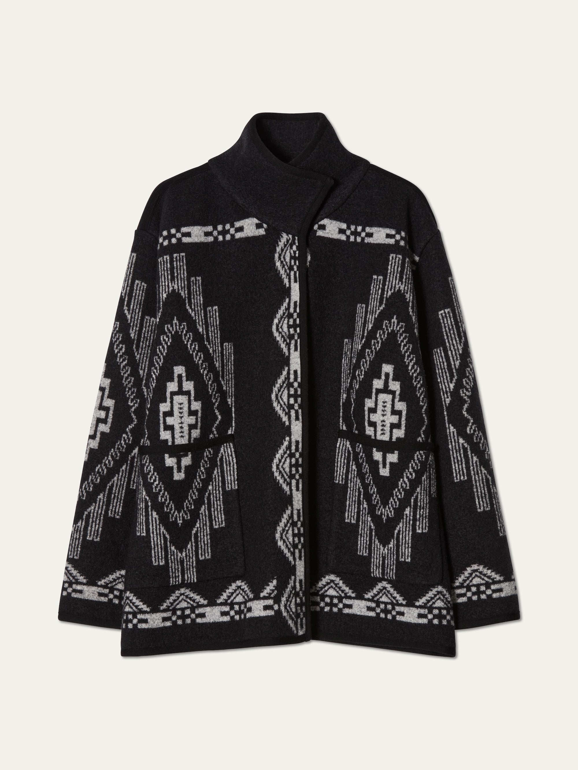 The We Norwegians Kautokeino Jacket for women is a black boiled wool jacket with a geometric white and gray Southwestern-inspired jacquard pattern, featuring long sleeves, front pockets, and a high collar.
