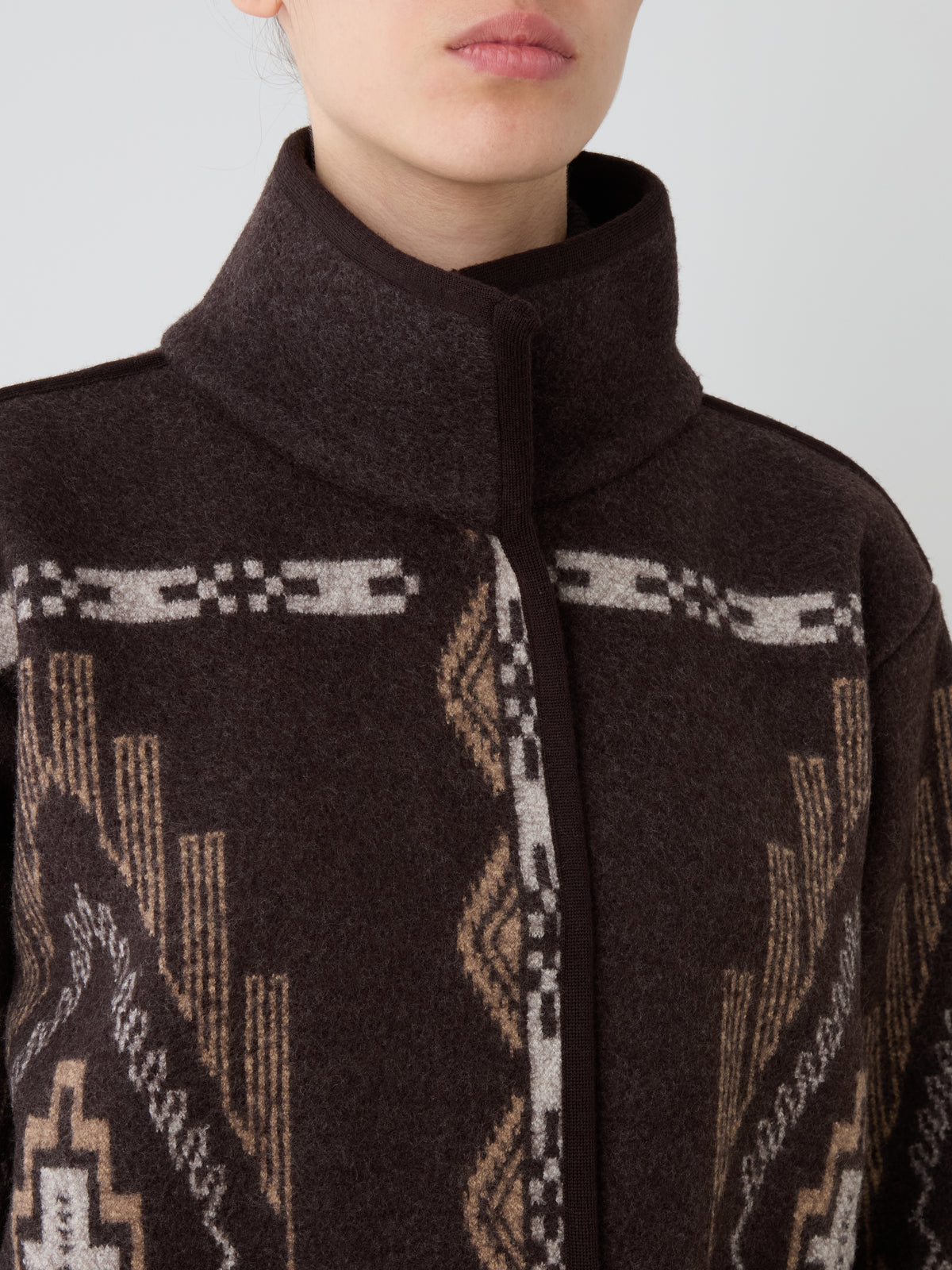 An oversized We Norwegians Pioneer Jacket women in dark brown boiled wool with a high collar and a geometric pattern in tan, white, and grey.