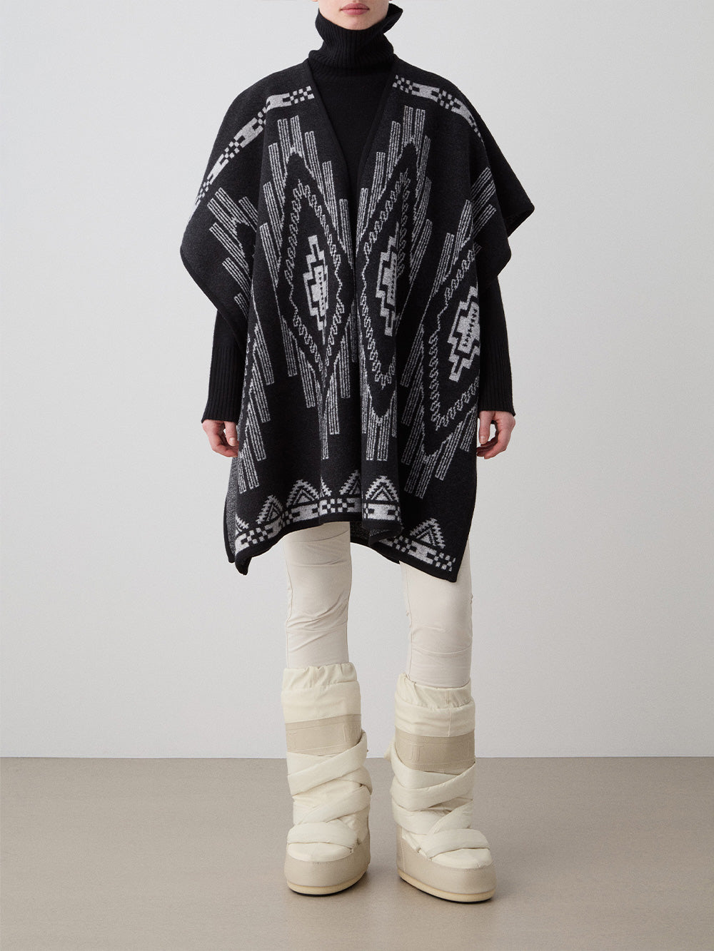 We Norwegians_FW25_Women | Model is wearing the Kautokeino poncho | Black in color with a jacquard pattern inspired by Native and Indigenous American art | Made with boiled merino wool | Front view against a white background