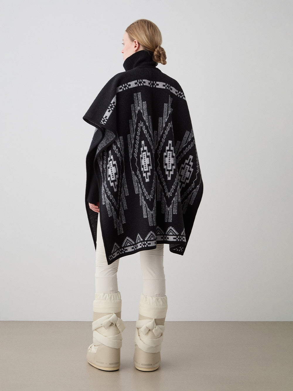 We Norwegians_FW25_Women | Model is wearing the Kautokeino poncho | Black in color with a jacquard pattern inspired by Native and Indigenous American art | Made with boiled merino wool | Back view against a white background