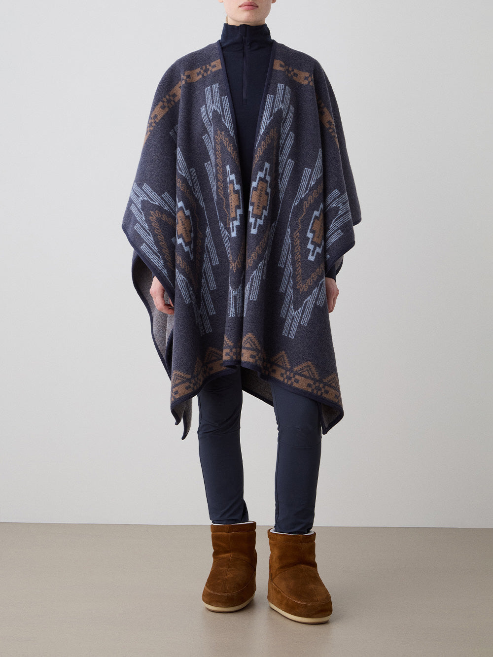 We Norwegians_FW25_Women | Model is wearing the Kautokeino poncho | Navy Blue in color with a jacquard pattern inspired by Native and Indigenous American art | Made with boiled merino wool | Front view against a white background