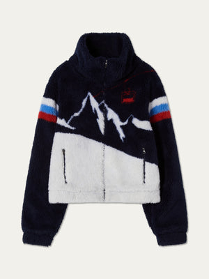 The We Norwegians Snowmass Jacket for women is a navy and white jacquard fleece with a zip-up front, mountain graphic, red and blue striped sleeves, high collar, and two zippered pockets—an après-ski essential.