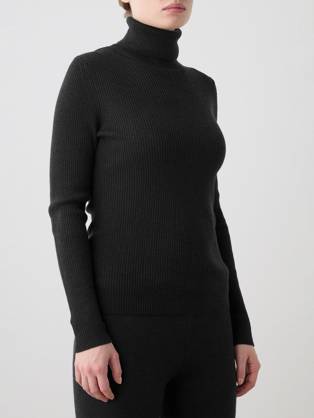 A woman wearing the We Norwegians Geilo TurtleNeck and matching black pants stands against a plain light gray background.
