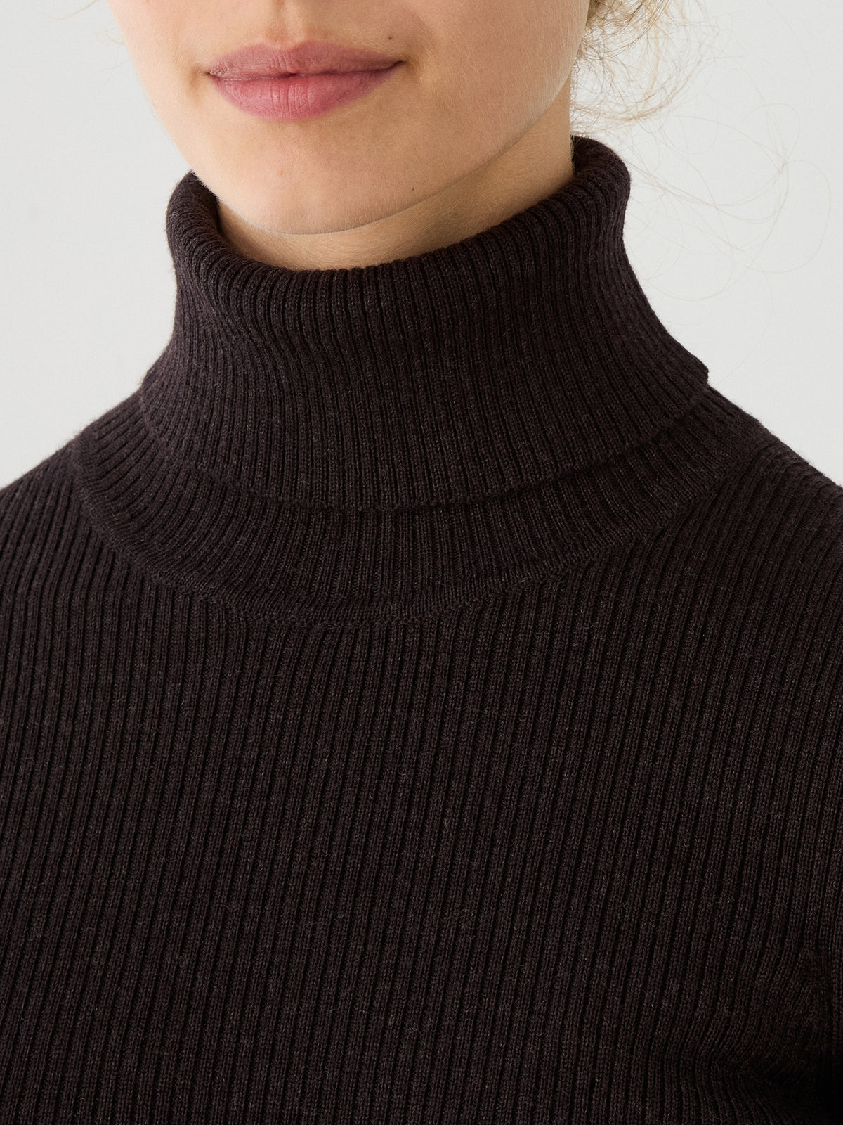 A close-up of a person wearing the Geilo TurtleNeck for women by We Norwegians, a ribbed dark brown roll neck sweater crafted from soft merino wool. Only the lower half of the face, neck, and upper chest are visible.