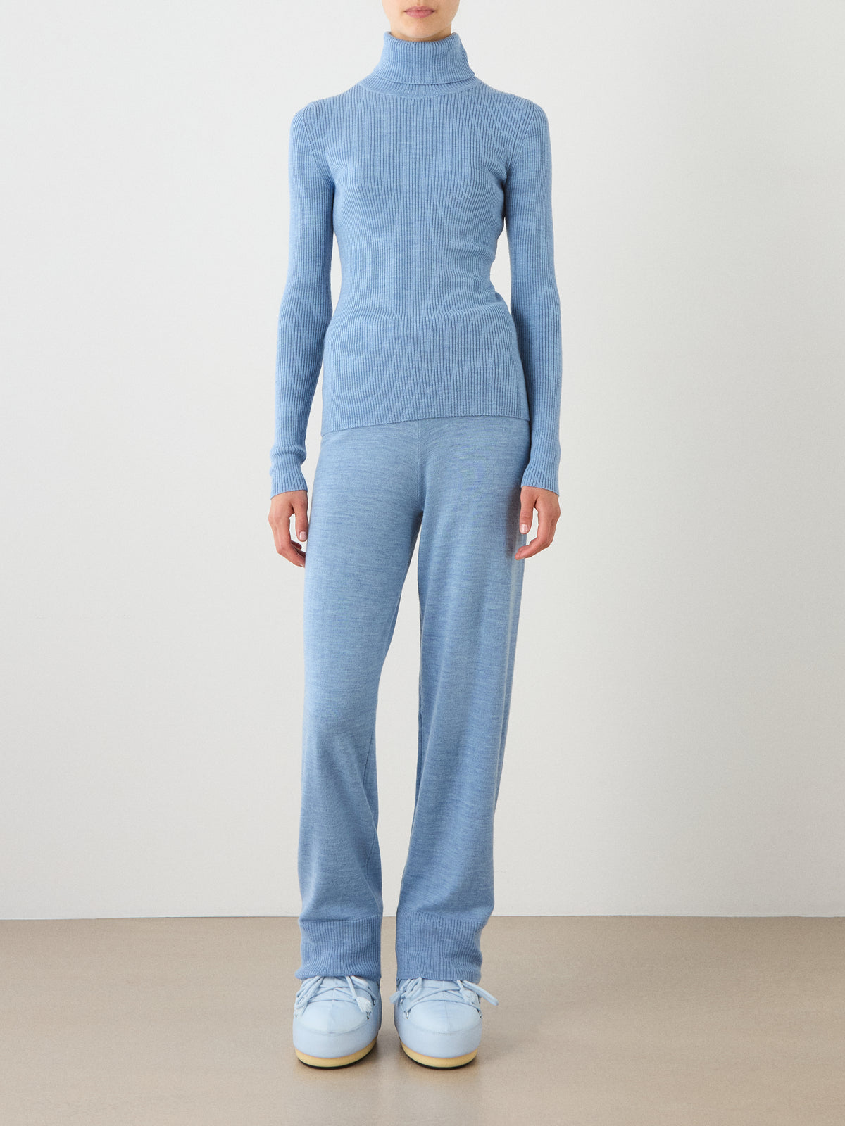 A person stands against a plain background wearing the Geilo TurtleNeck women sweater by We Norwegians in light blue, paired with matching blue pants and light blue platform shoes. The outfit looks soft, cozy, and casual. The person’s face is not visible.