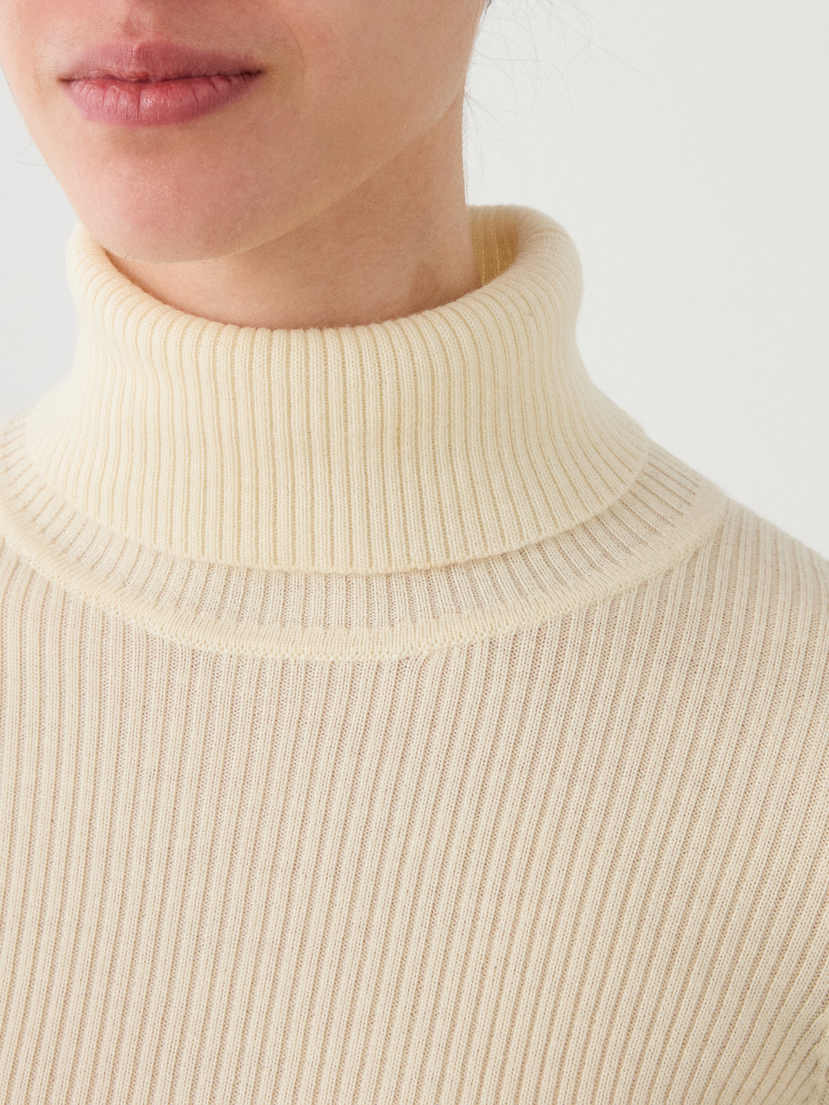 A close-up of a person wearing the We Norwegians Geilo TurtleNeck for women in cream, highlighting their lower face, neck, and the ribbed texture of the fabric.