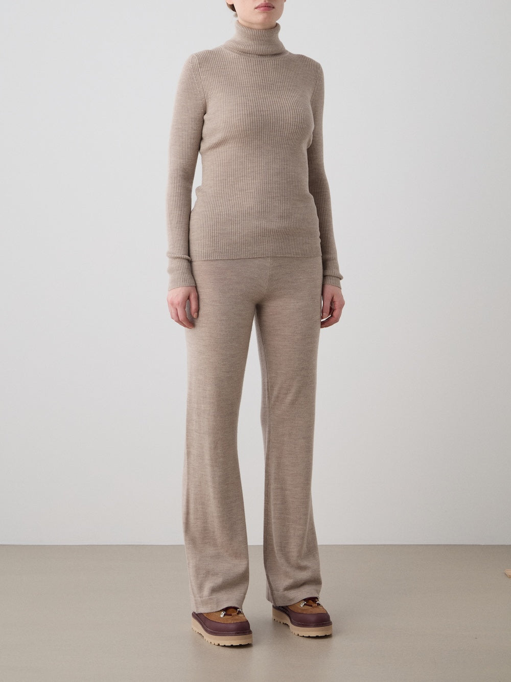 Person wearing a beige knit outfit with a plain background