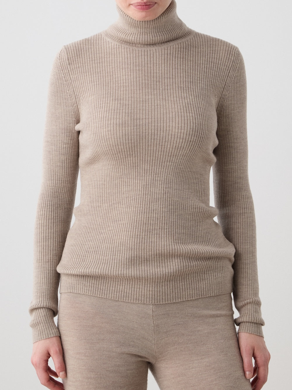 A woman wearing the We Norwegians Geilo TurtleNeck in beige merino wool with matching pants stands against a plain light background.