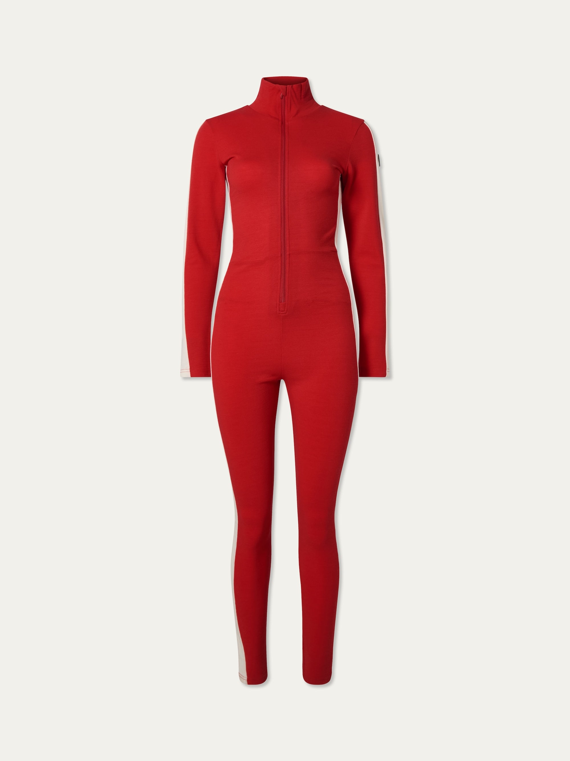 The We Norwegians Voss Jumpsuit women is a fitted, long-sleeved red retro piece with a high collar, front zip, and white stripes on each leg. Ideal for ski loungewear, it's shown against a white background.
