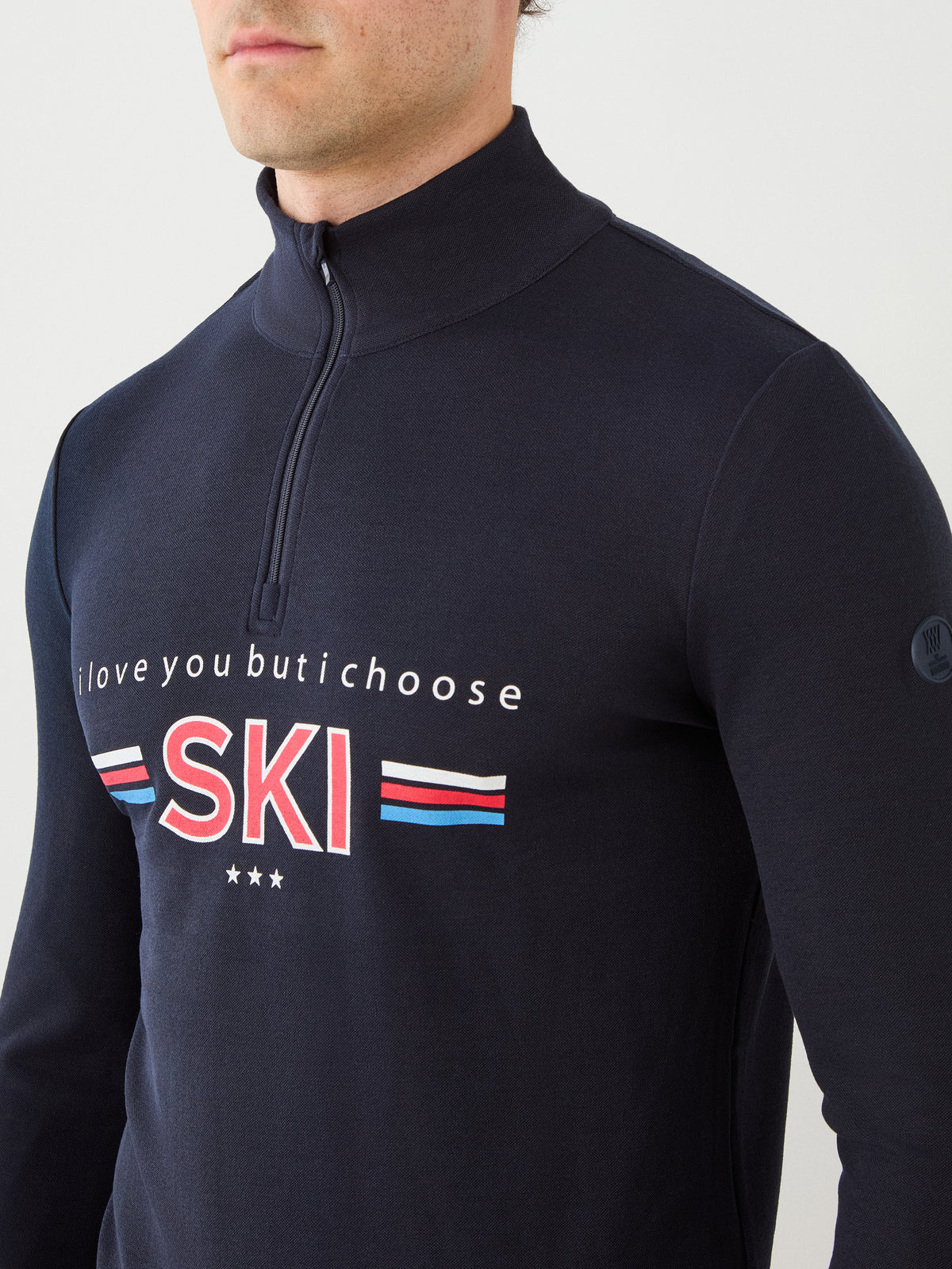 A man wearing the We Norwegians Moore ZipUp men’s navy quarter-zip shirt featuring “I love you but I choose SKI” text and red, white, and blue stripes across the chest.